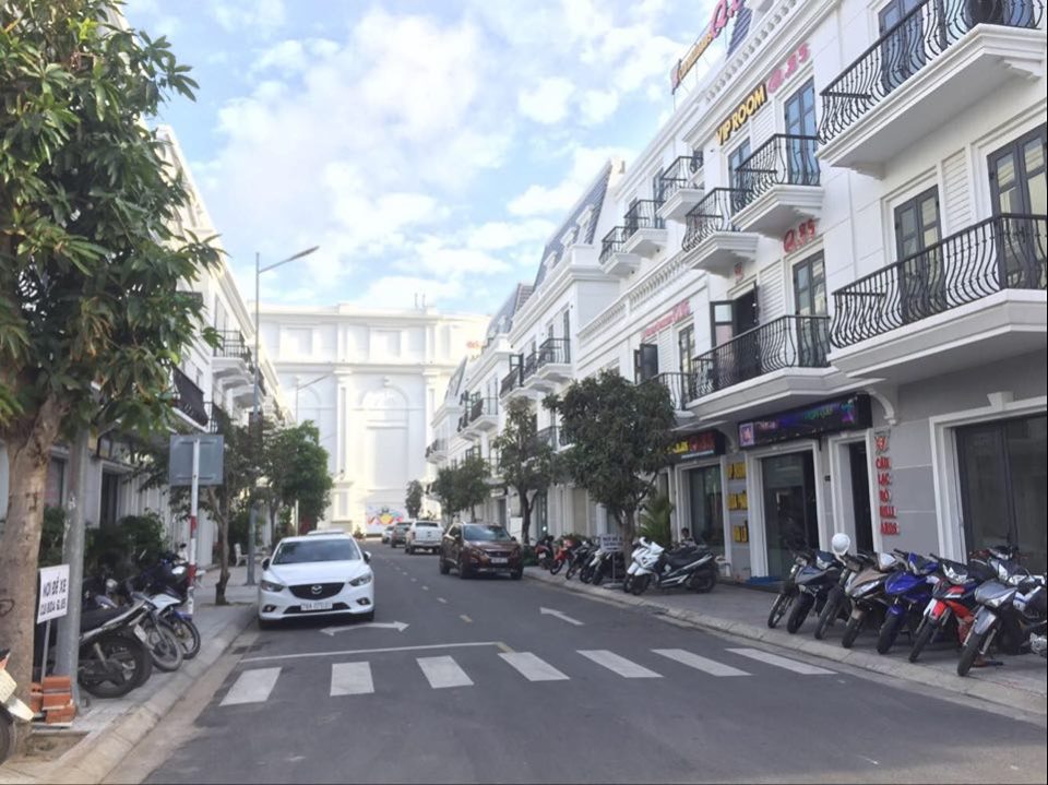 Một dãy nhà phố thương mại, bên dưới là đường, nhiều xe máy trên vỉa hè, ô tô chạy trên đường