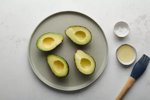 Cắt đôi quả bơ theo chiều dọc. Lấy ra khỏi hố và ngay lập tức phủ lên thịt quả bằng nước vôi tươi. Bơ cắt nửa quả đã loại bỏ các vết rỗ Đánh một ít dầu ô liu lên bề mặt của mỗi quả bơ và rắc muối lên.