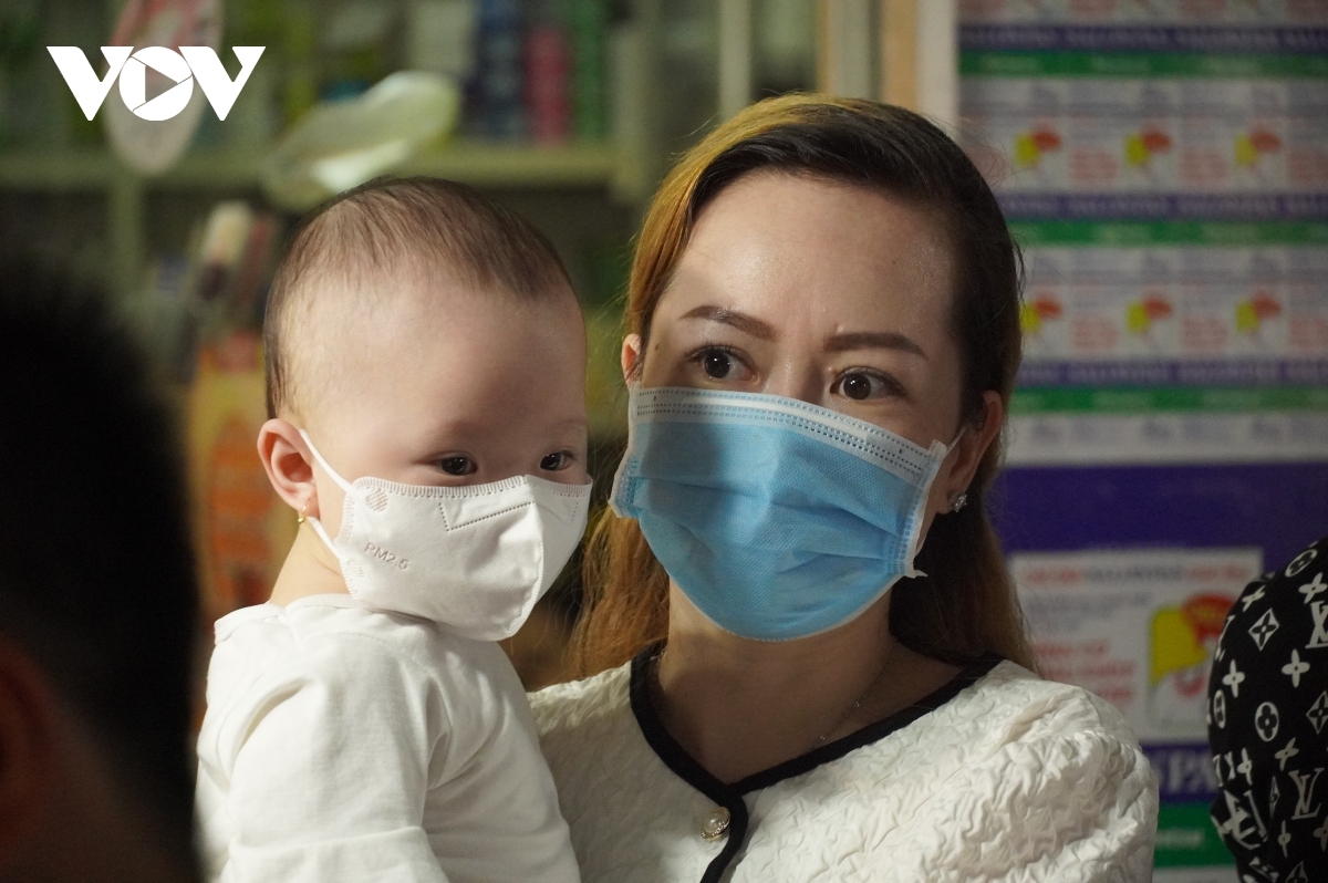 Some parents carrying their children stand still as they wander around the crowded street.