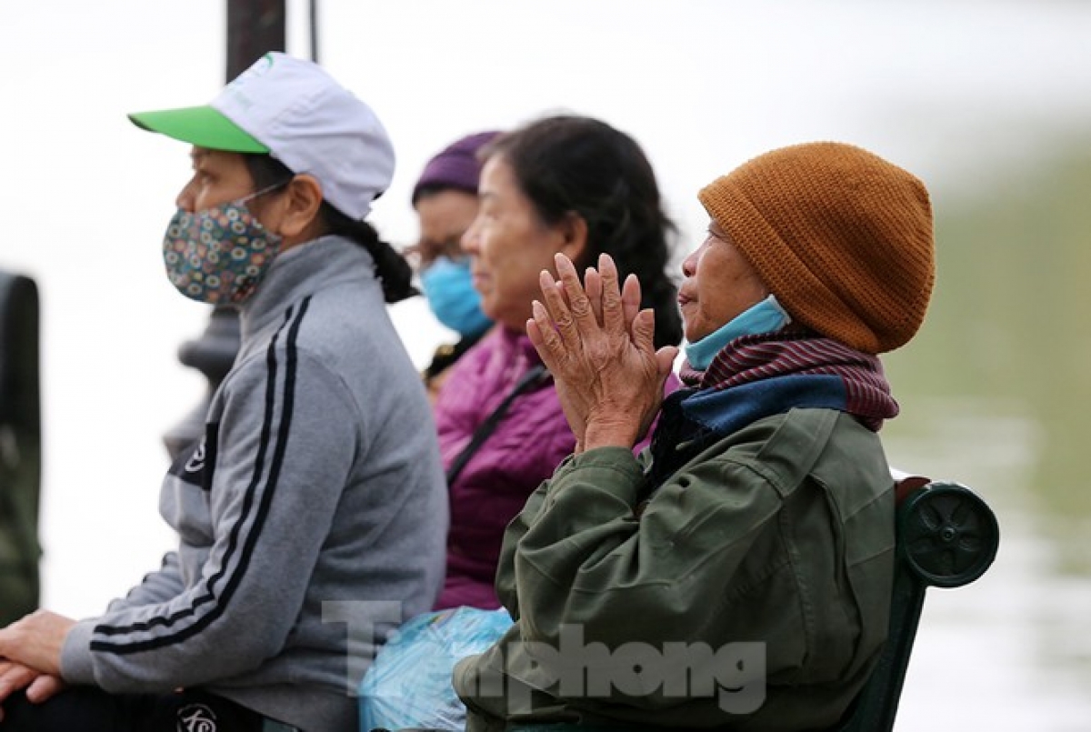 An old woman wraps up tight in woolen hat and scarf whilst rubbing her hands to deal with the cold weather.