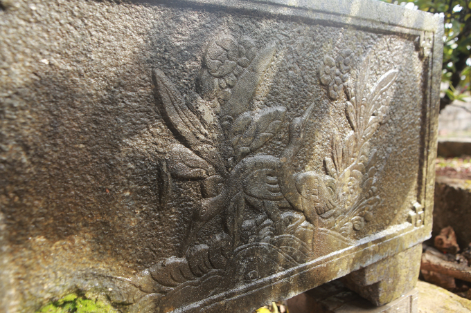 Một bên bể được khắc hình hai con hạc, một con ngửa mặt lên trời, một con đang mò., phía trên có hoa an lạc trắng, lá dài thường hay trồng ở đình, chùa