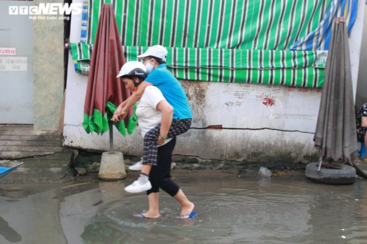 Hai người phụ nữ cõng nhau qua đoạn nước ngập.