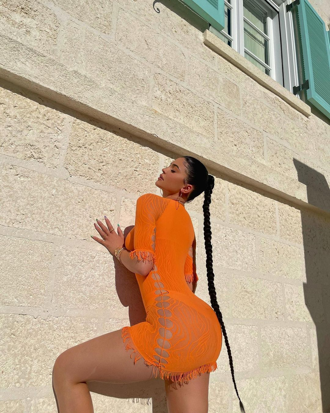 Kylie Jenner struck a sun-kissed pose in her vibrant see-through orange dress with side cut-outs